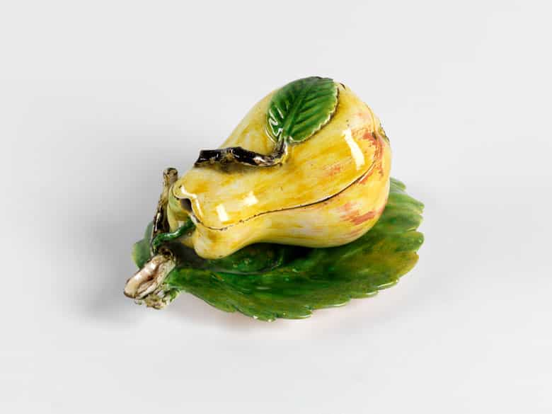 Detailabbildung: Fayence-Deckeldose in Form einer Birne auf einem großen Feigenblatt liegend