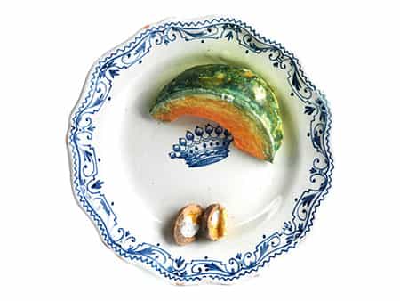 Fayence-Schaugerichtteller mit aufgeschnittenem Melonenstück und geöffneten Walnussschalen